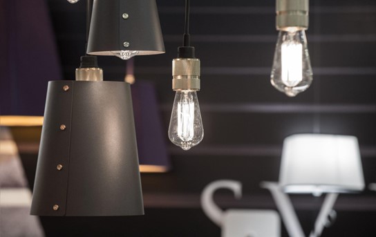 Close-up of assorted indoor lighting fixtures including a matte black lampshade,
a bare filament bulb, and a classic white lampshade against a dark purple backdrop.
